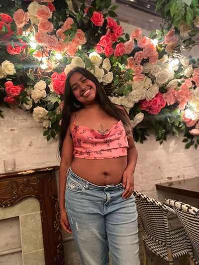 Yareimy is standing in front of a wall hanging made of roses 