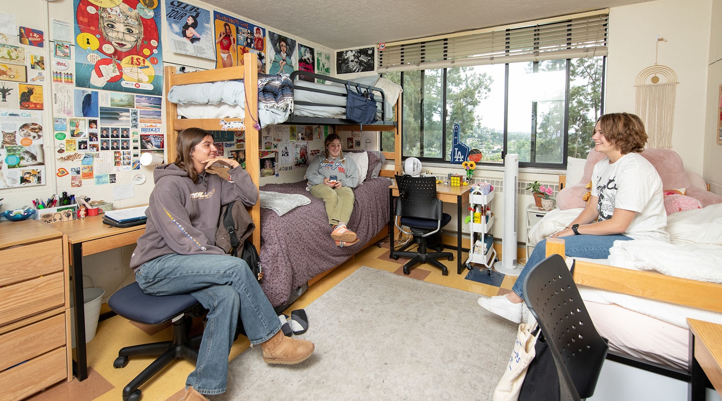 three students chatting together in a decorated dorm room