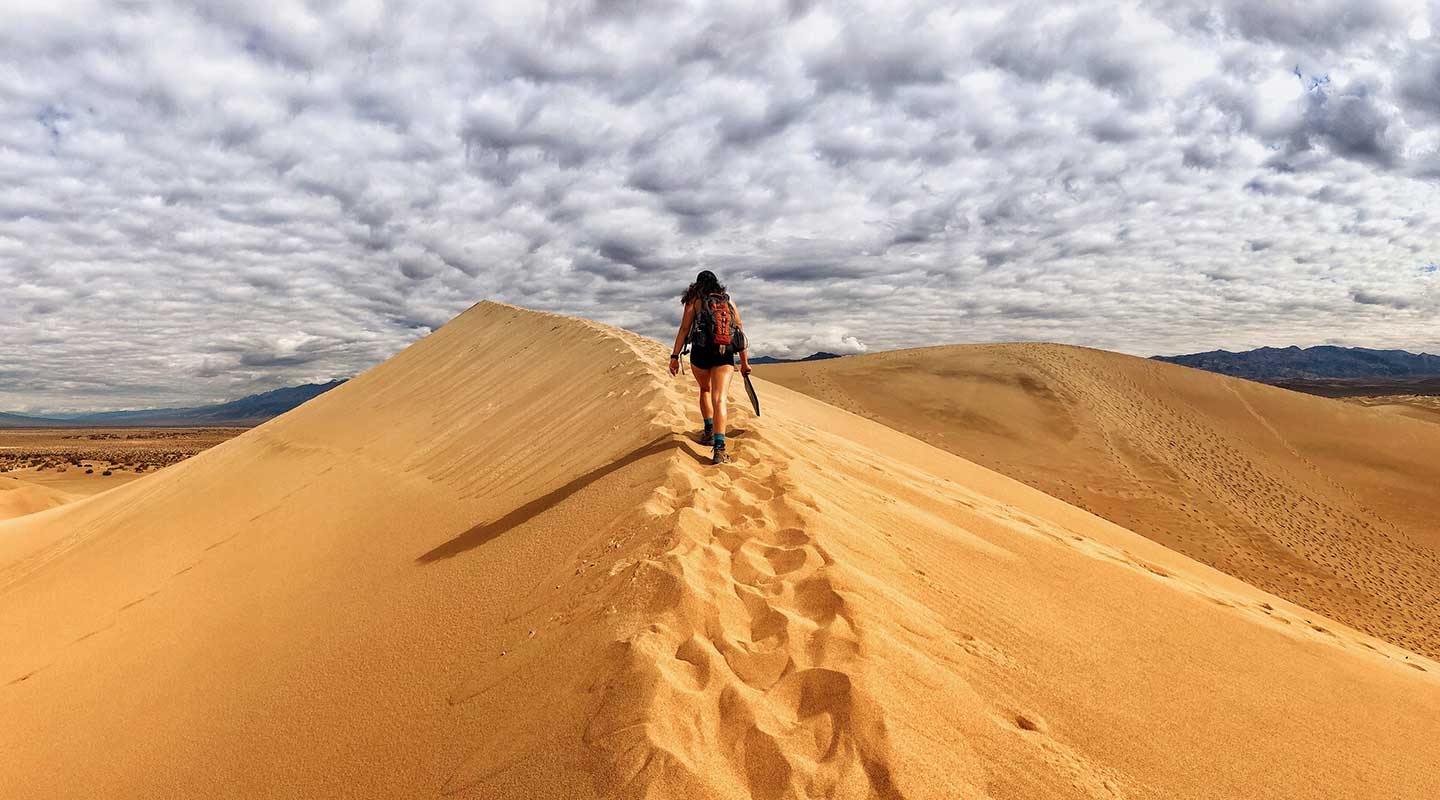 A student hiking along a sandy ridge in the desert with dramatic sky