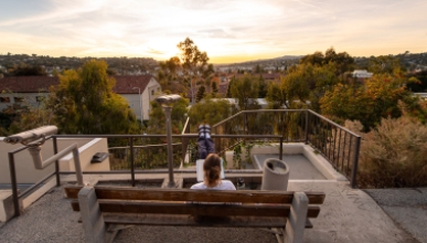 A view of a student on a bench overlooking campus from above at sunset