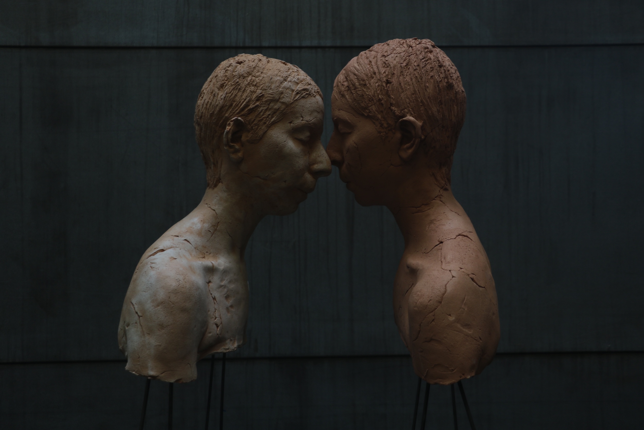 color image of two sculptural human busts in profile with faces touching