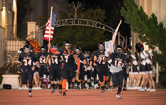 The Tigers charge onto Patterson Field prior to the start of their Homecoming contest in 2015. (The rally flag was the idea of Scott and his team- mates.) 