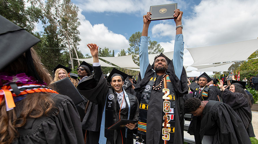 A new Occidental College grad proudly holds up his diploma on Commencement Day 2025