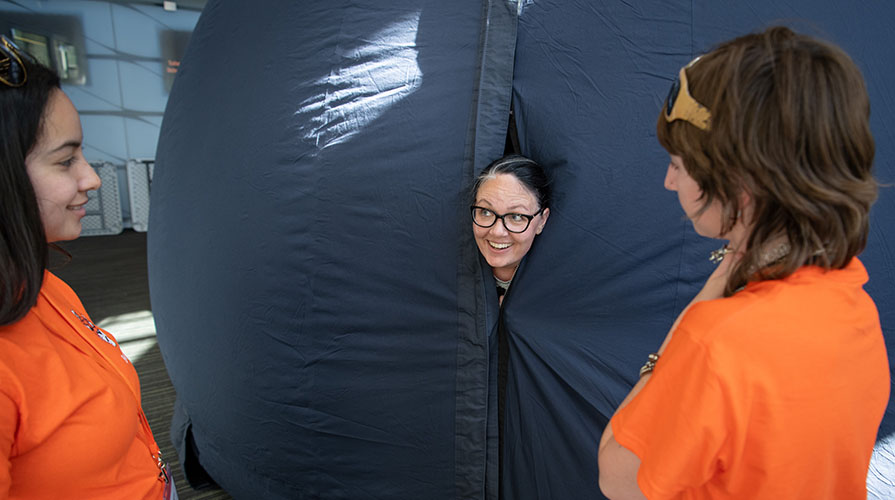 Professor Sabrina Stierwalt inside an inflatable solar system, sticking her head out with a smile