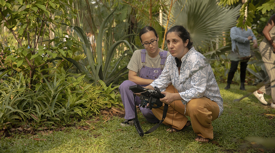 Anahid Yahjian, right, a female Armenian director crouching down with a coworker in a green outdoor setting