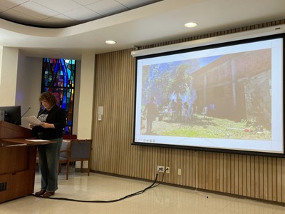 Professor Rebecca Bartel giving a lecture with an image on a screen behind her.