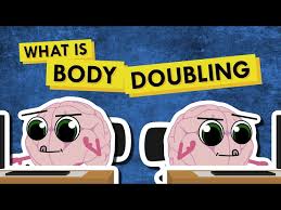 Two cartoon brains with big eyes sit at desks next to each other, representing body doubling. Above them, bold yellow and black text reads "What is Body Doubling" on a blue background.