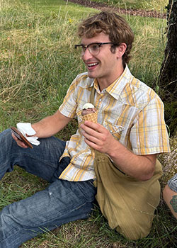 a young man with glasses holding an ice cream cone and sitting on the ground