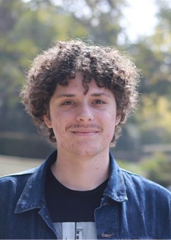 Eran is wearing a blue shirt and has short curly brown hair