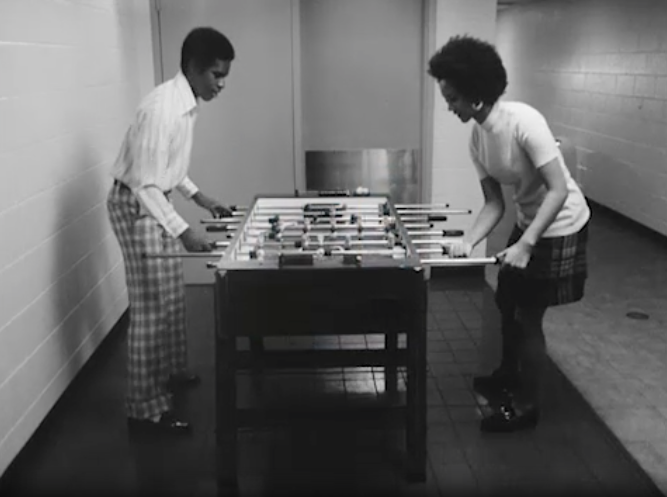 Black and white photograph of two Black people playing foosball 