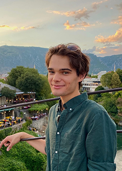Garret is standing in front of greenery and a mountain in the background