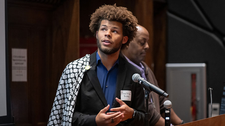 Jaymes Griggs in front of a microphone with a blue shirt and sweater, looking upward