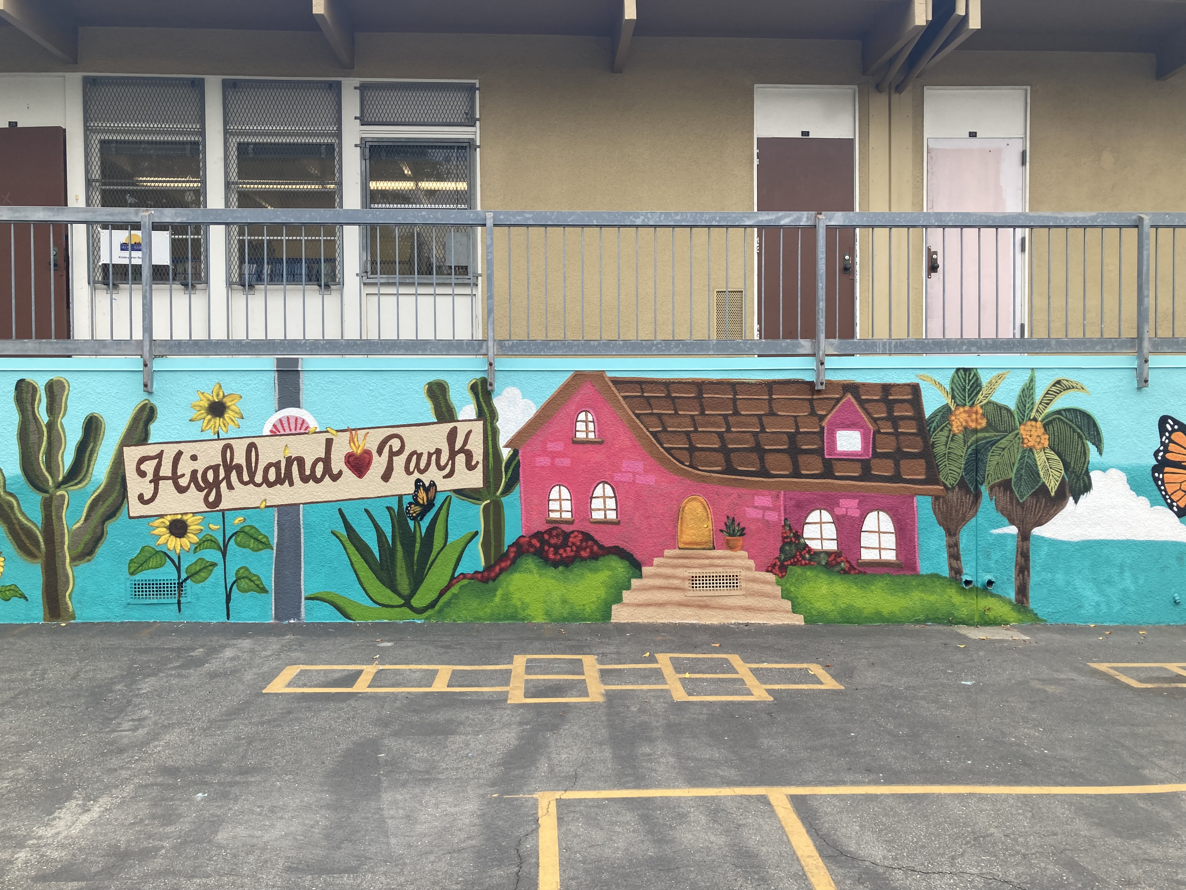 Colorful photograph of a wall with a mural painted on it depicting a pink house and a sign that says &quot;Highland Park&quot;