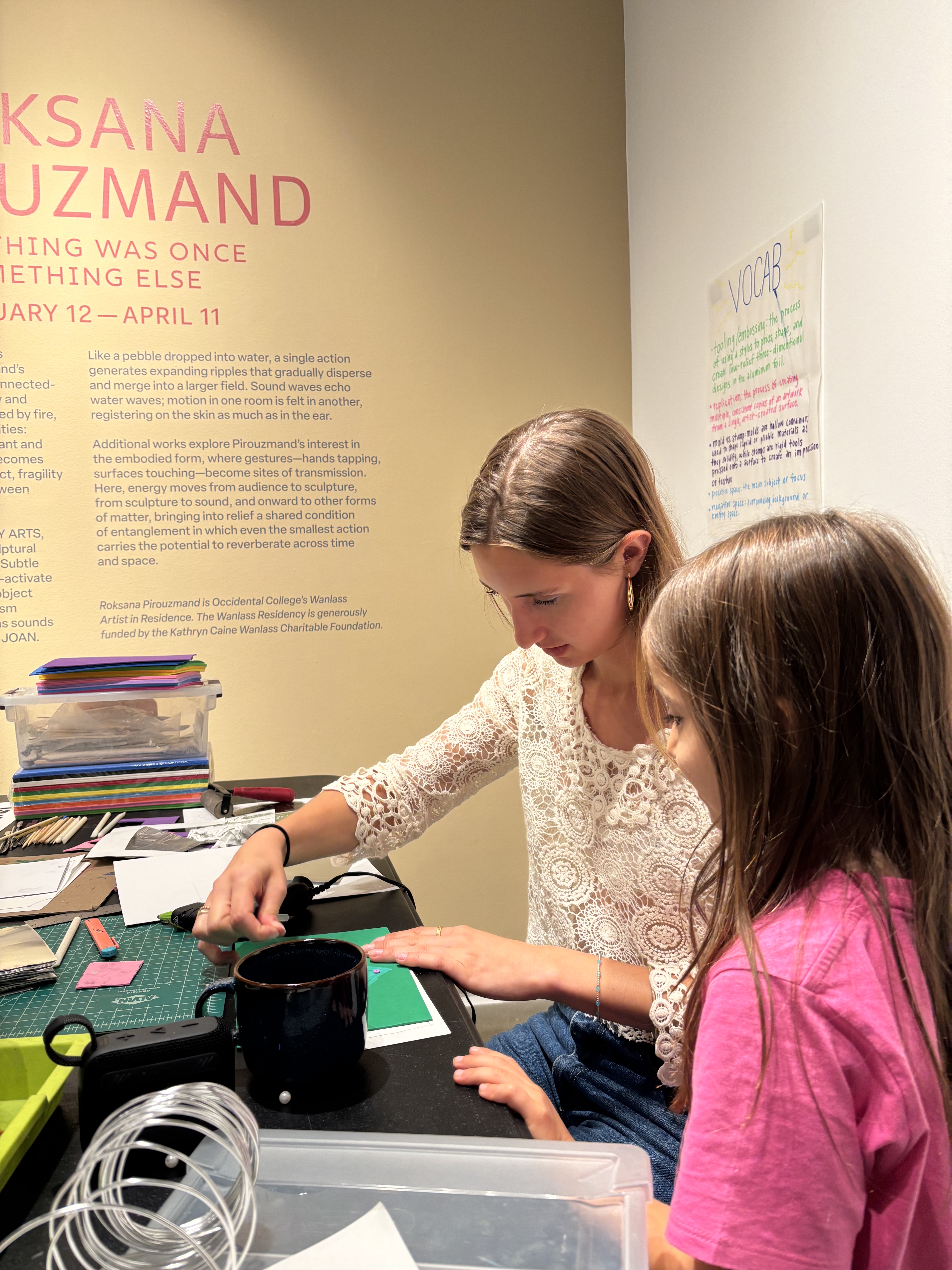 Two people are creating an art project together in a gallery space. One is older and one is younger. 