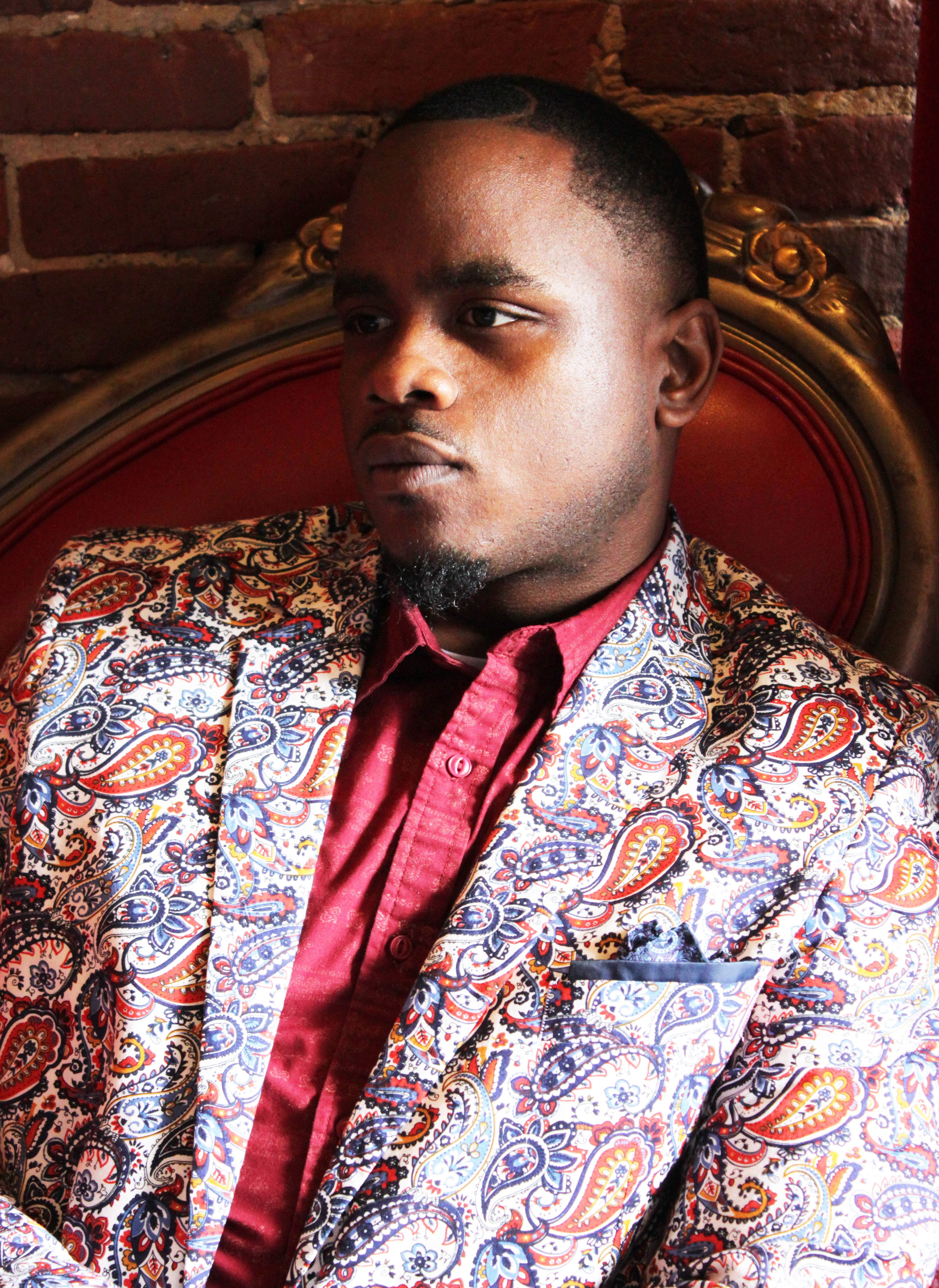 Jonah M-W_X_Marsha E. Eagle.jpg Portrait of Jonah Mixon-Webster, he is wearing a floral print suit and a pink shirt, looking into the distance.