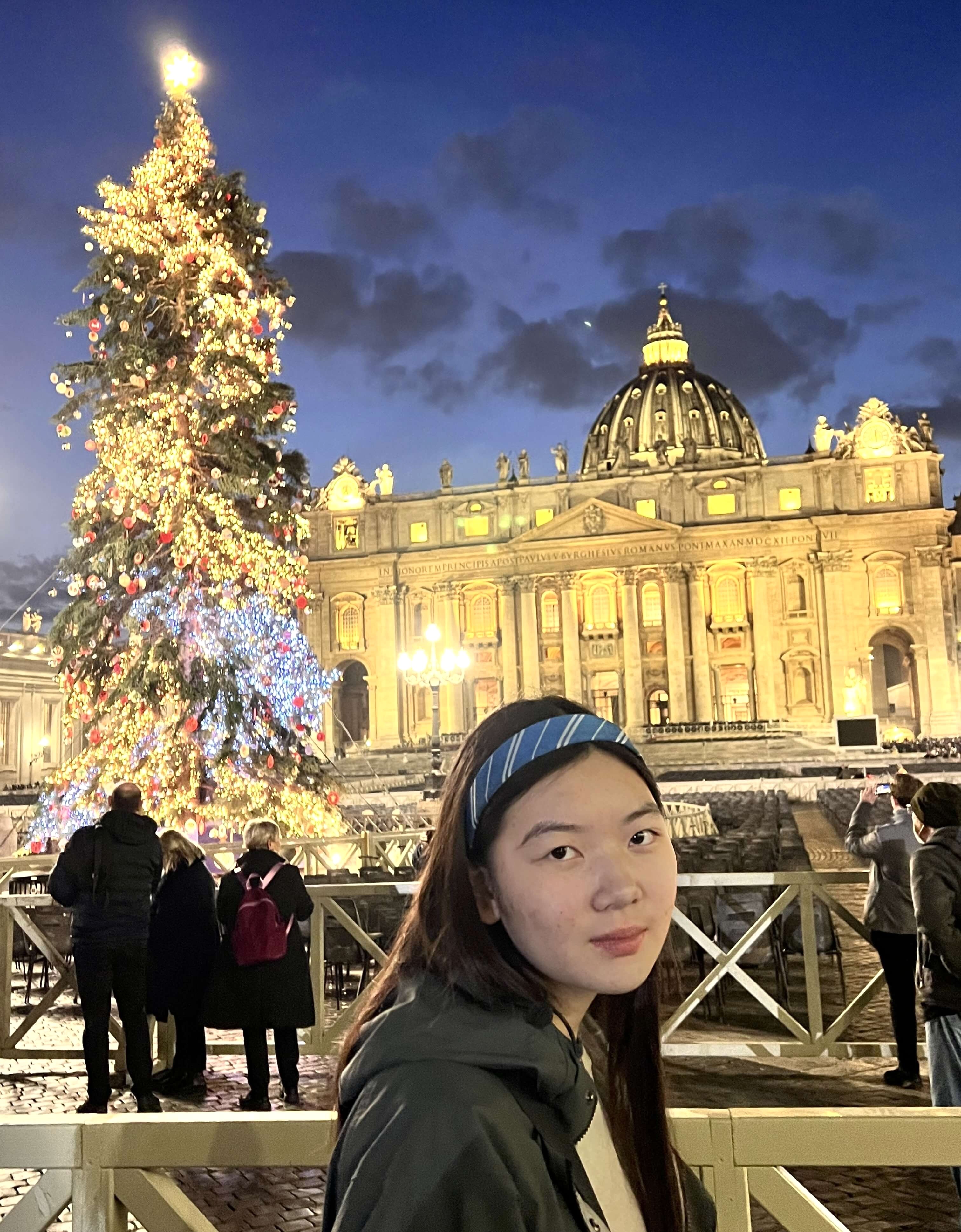Maggie in front of an illuminated St. Peter's Basilica and Christmas tree.