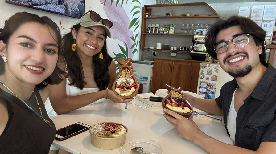 Three Oxy student sitting at a table eating a meal and smiling at the camera
