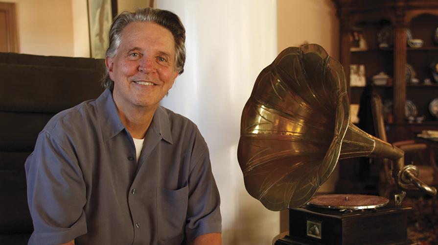 Mike Curb in a grey shirt sitting next to a gold grammophone