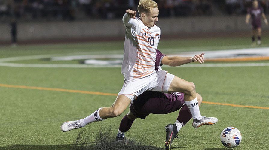 An Oxy soccer player hangs suspended in the air as he goes to kick the ball