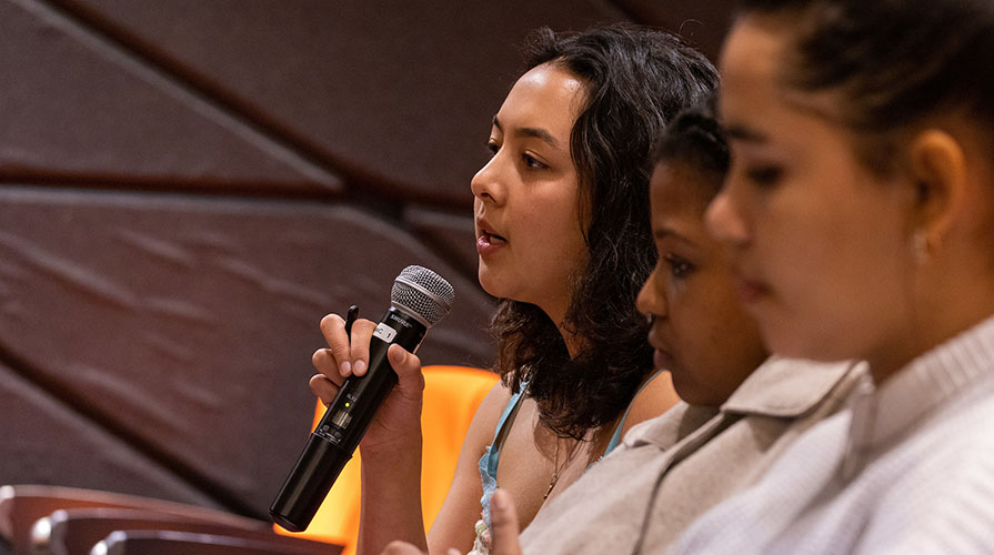 three seated students, one holding a mic and asking a question