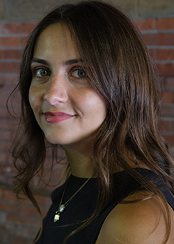 Nora has dark brown hair and is looking at the camera from the side