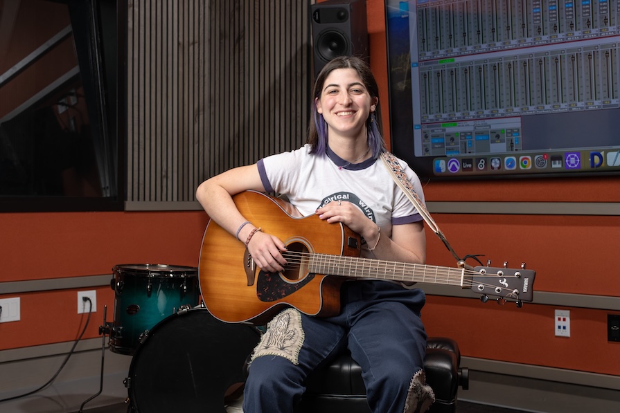 an occidental student posing for photo with guitar inside of music studio