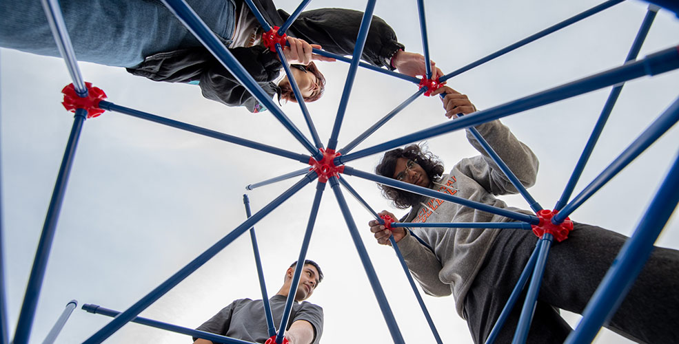 three students shot from below, constructing the Oxyhedron structure