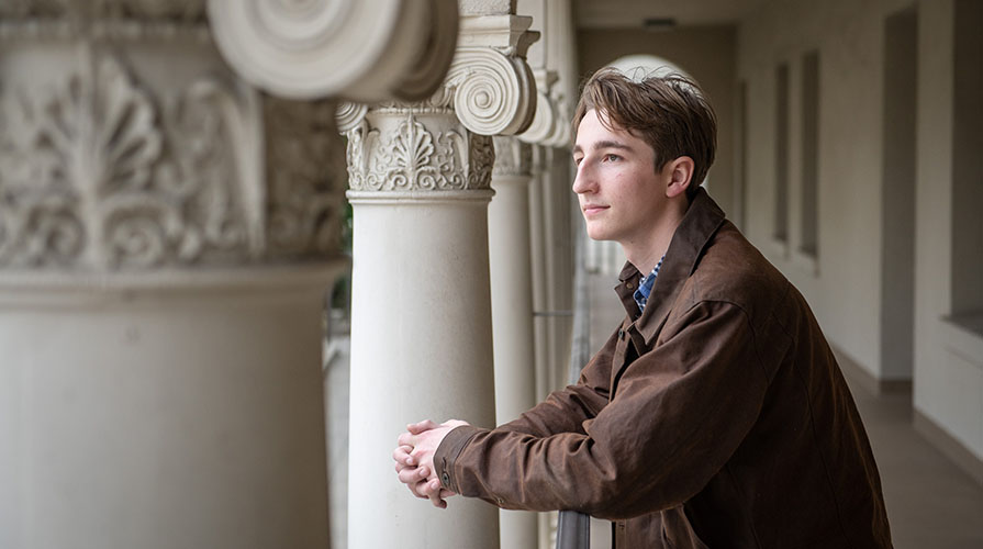 Will McMillan in profile, standing against Greek columns on campus