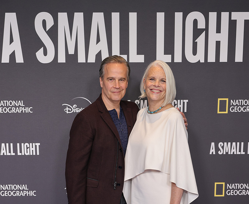 Two writers stand/pose next to each other at an industry event