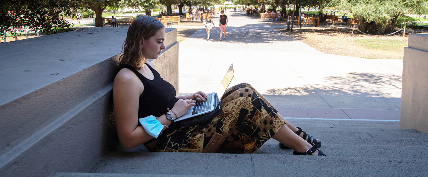 A student studying with her laptop by the library