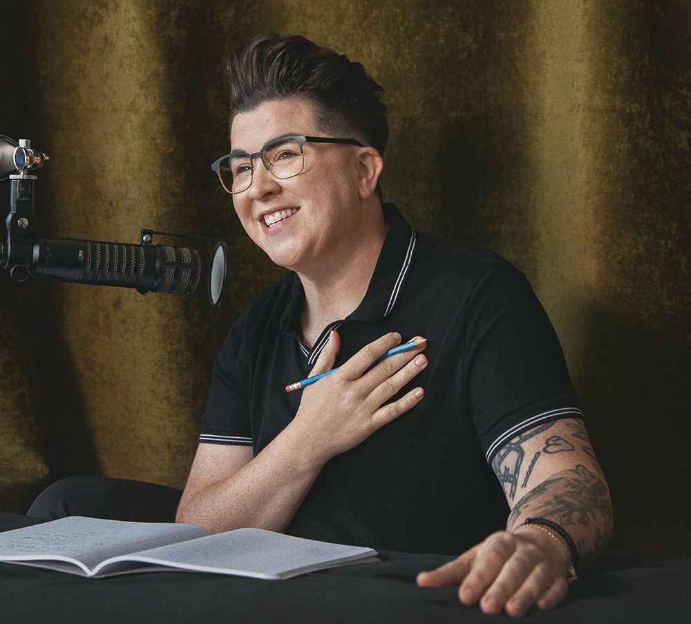 VSpehar_Patreon.jpg medium of V Spehar smiling with hand to chest and podcast microphone camera left