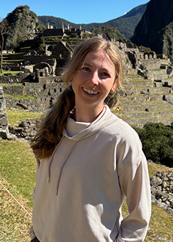 Chloe is standing with greenery and a mountain in the background