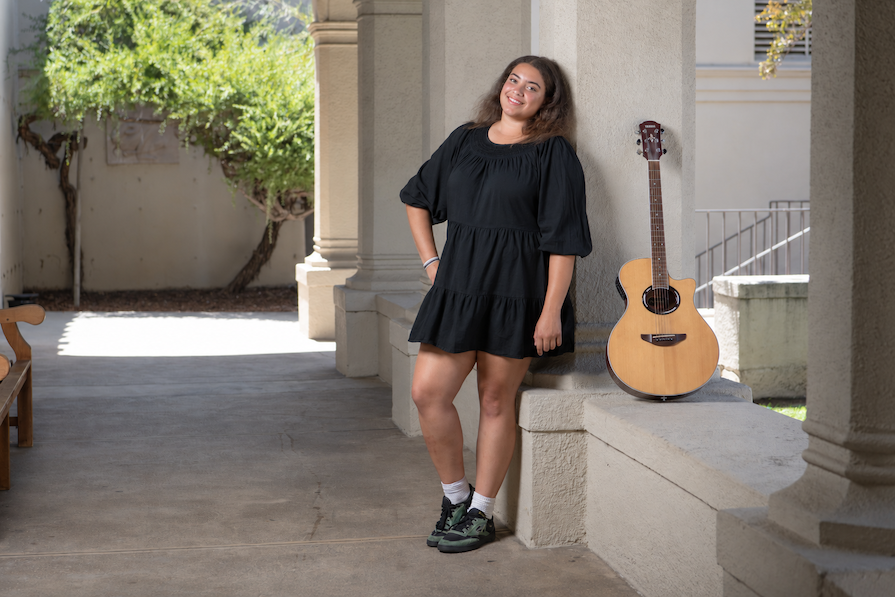 Occidental Student posing for photo on the Los Angeles Campus standing next to their guitar