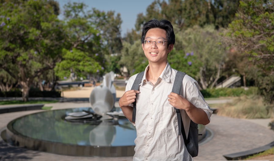an occidental student poses for a picture in the Academic Quad with Gilman Fountain in the background.