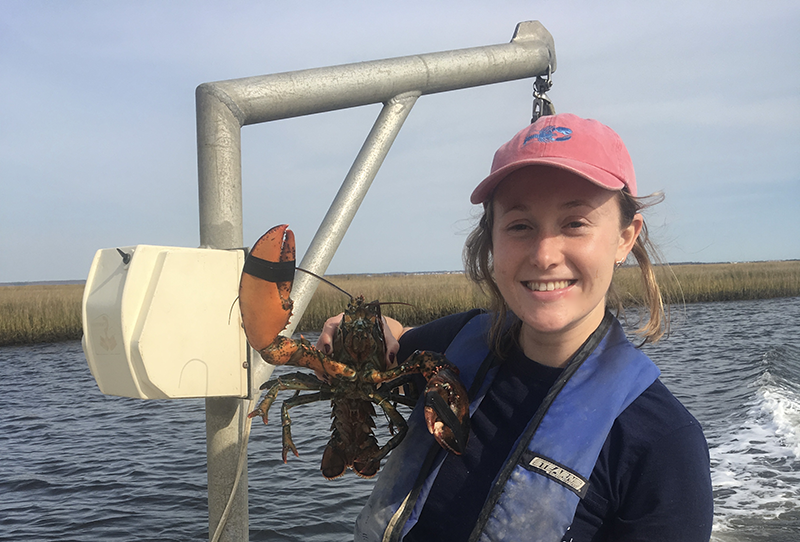 Zoe Kitchel stands on a boat holding a lobster specimen