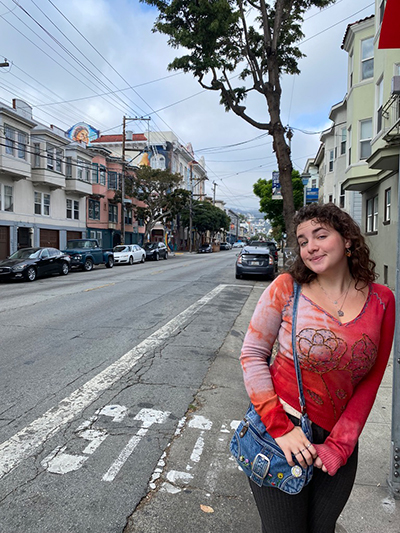 Barret is standing on a street with buildings and a tree in the background