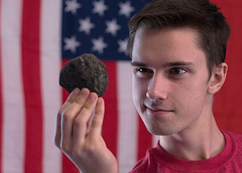 A photo of Occidental college student Matt Aleksey holding a rock against the back drop of an American flag