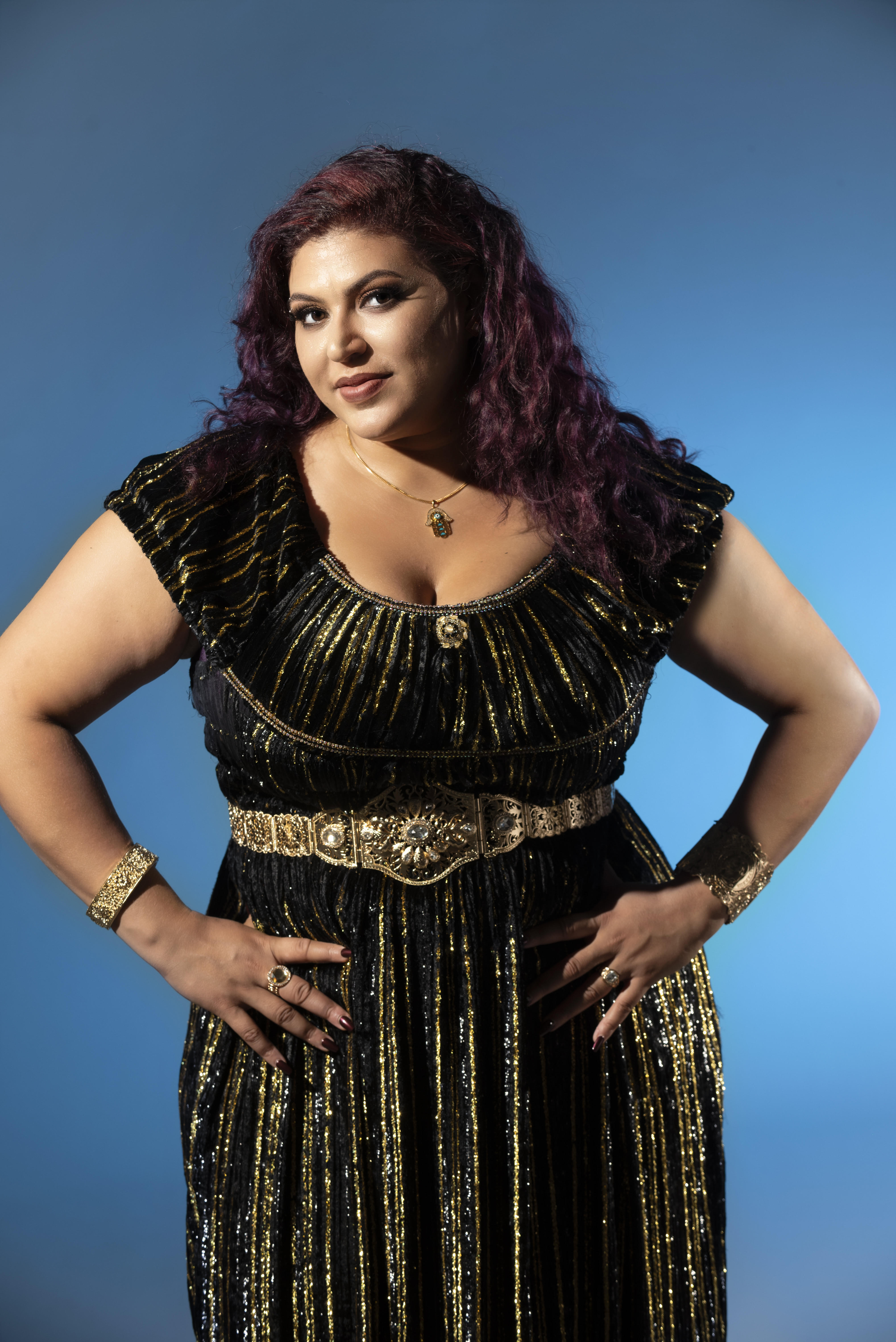 unnamed-1.jpg Esraa wearing a black dress with her hands on her hips against a blue background