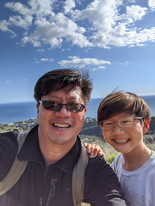 Chris Kim, Choi Family Director of Instrumental Music, hiking with his son Ian near the Pacific Ocean
