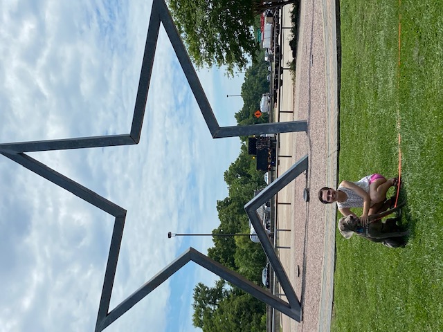 Deirdre Ellis with a dog kneeling in front of a large star sculpture 