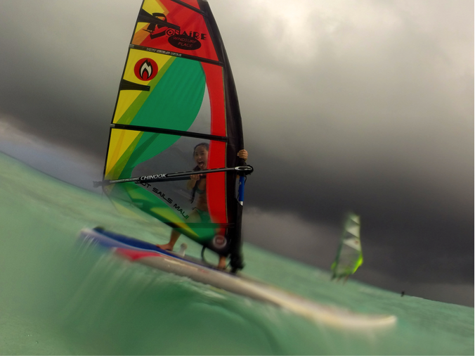 A windsurfer on a board with a colorful rainbow sail