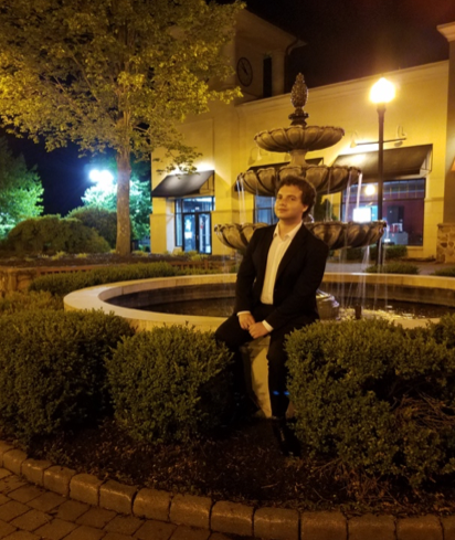 Brandon Markson sitting outside next to a water fountain