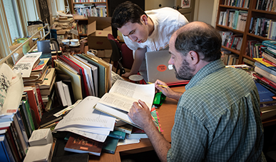 Teacher and student look at textbook together, surrounded by other books.