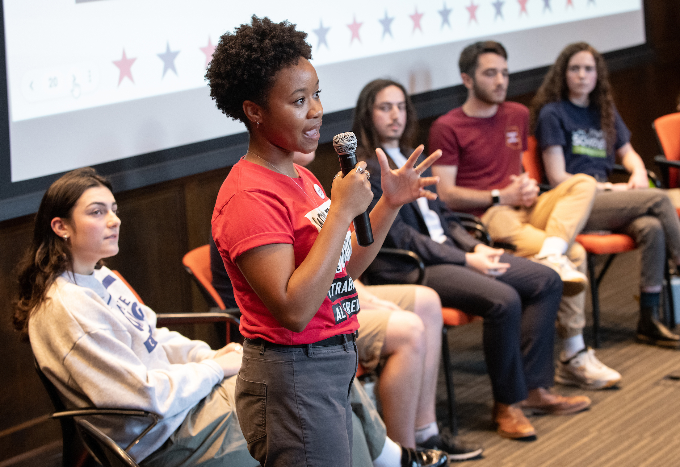 Previous campaign semester students sitting down, one standing holding a microphone.