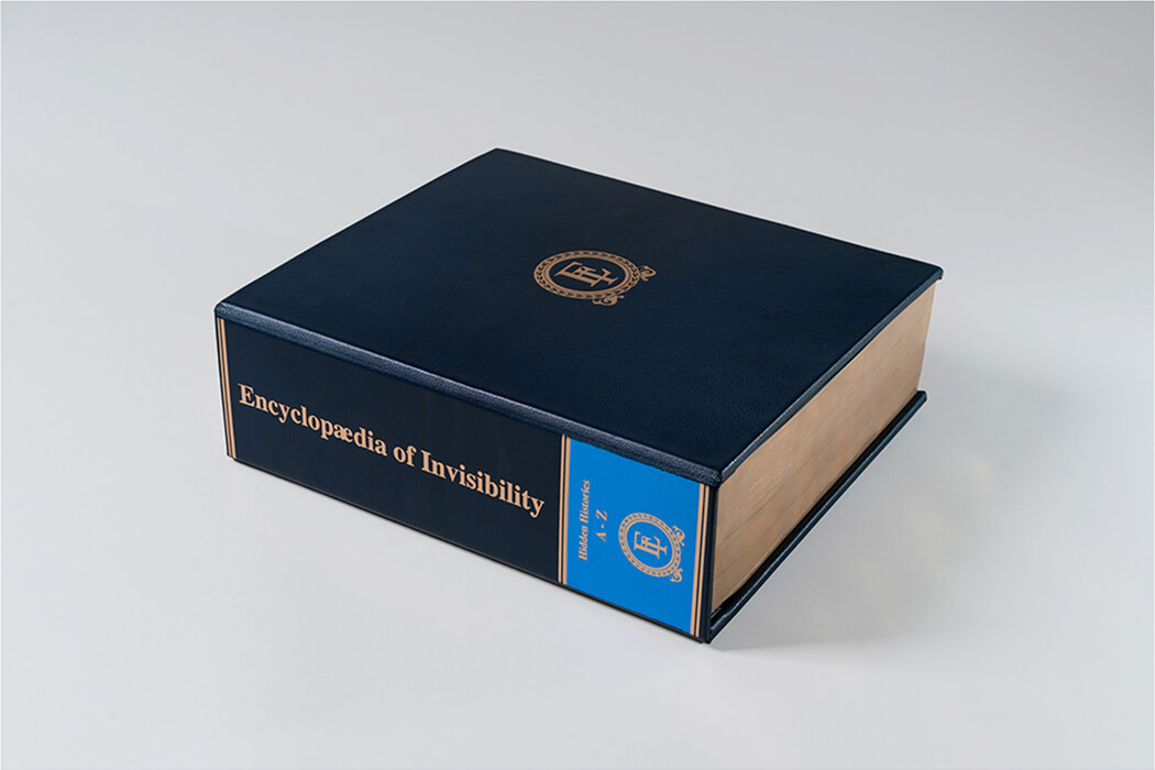 encyclopedia_of_invisbility_1050x700.jpg Photo of a blue leather bound book on a light grey background.
