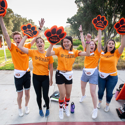 Oxy students in orange T-shirts and tiger paws shout and celebrate