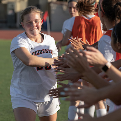 Woman athlete high fives a row of other athletes after a game