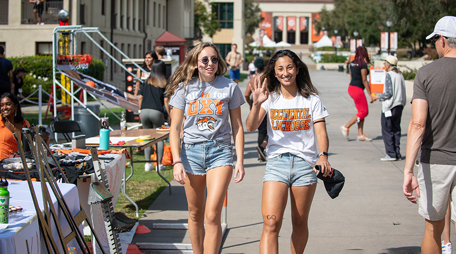 Two students wearing Oxy T shirts walk and wave, backed by Thorne Hall