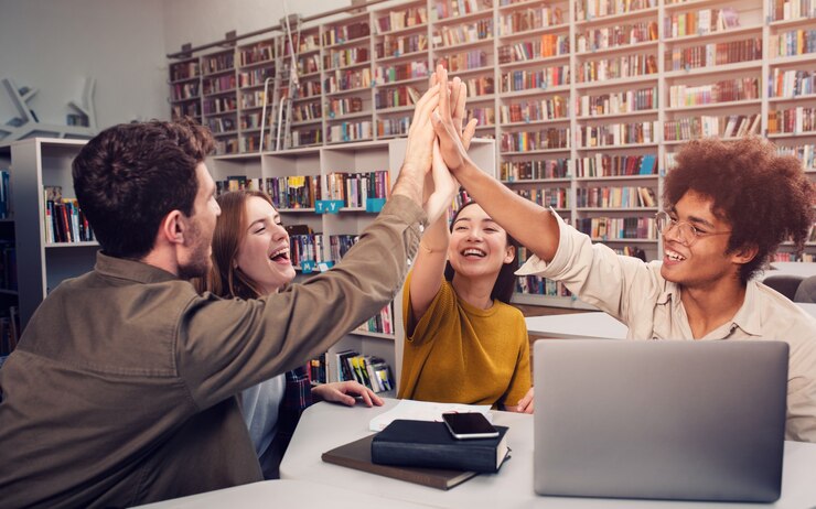 Group of four students giving celebrating with high-fives in a library