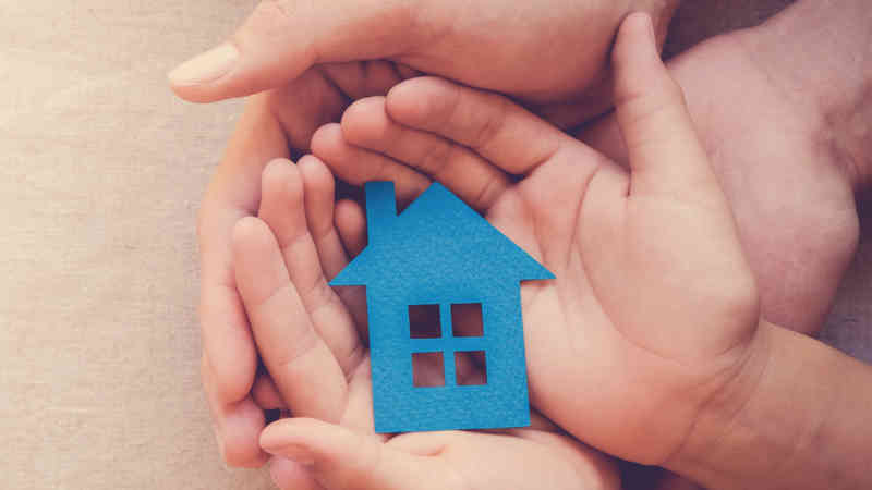 many hands hold a blue house-shaped cutout.